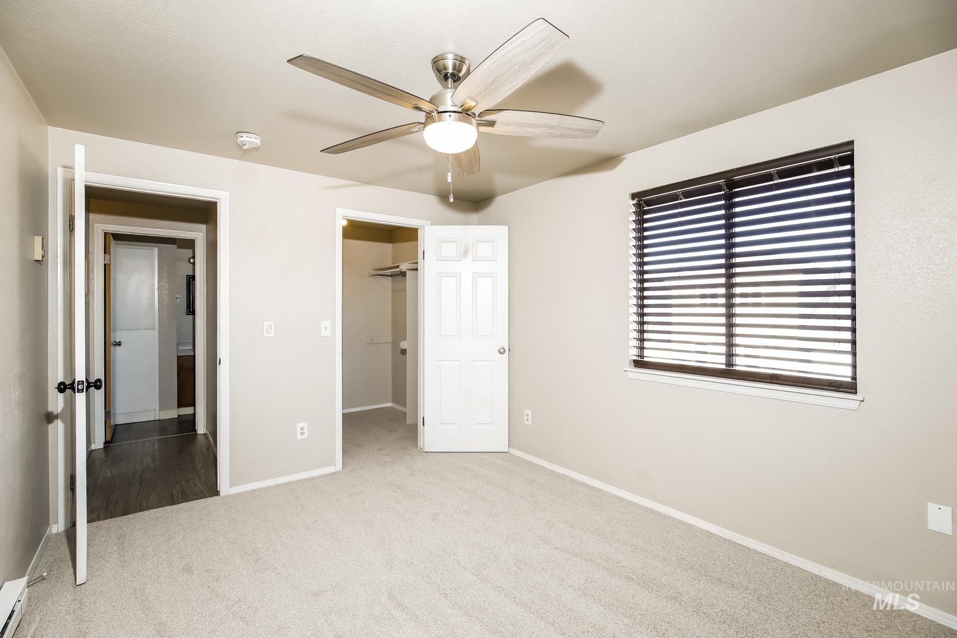 Unfurnished bedroom with a walk in closet, carpet floors, ceiling fan, and a baseboard radiator