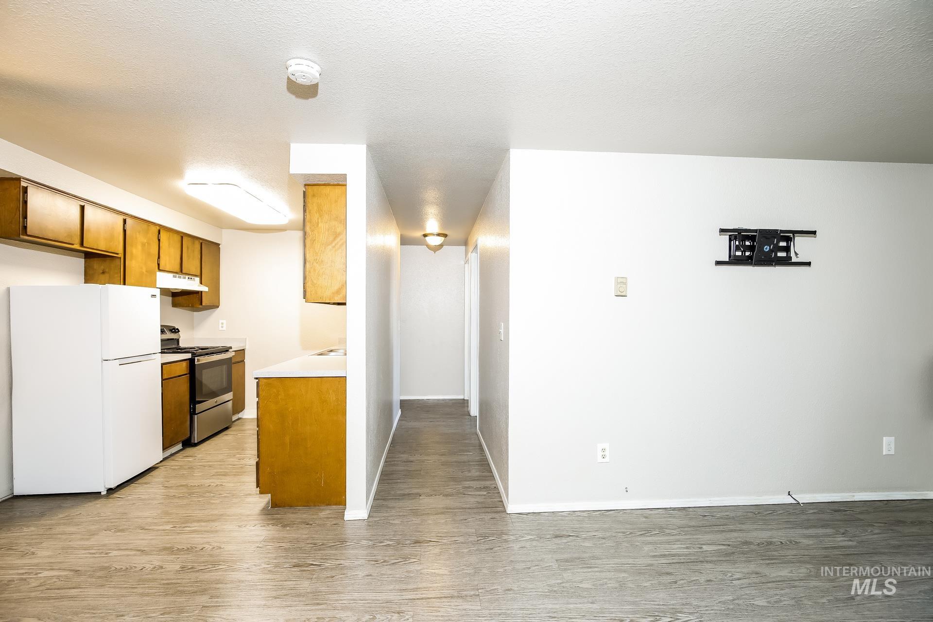 Kitchen with freestanding refrigerator, brown cabinets, light countertops, electric stove, and light wood finished floors