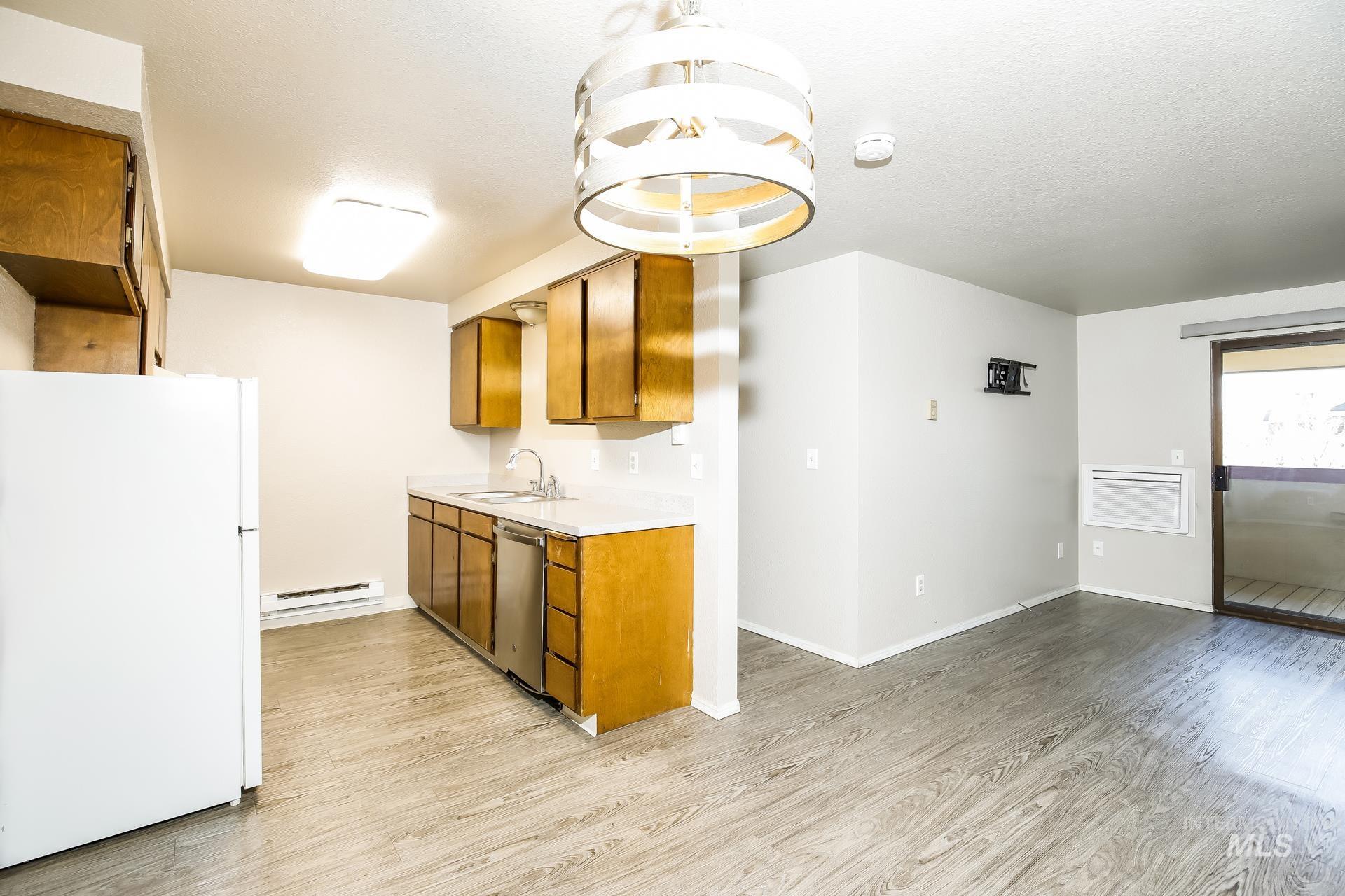 Kitchen with freestanding refrigerator, light countertops, brown cabinetry, light wood-type flooring, and dishwasher