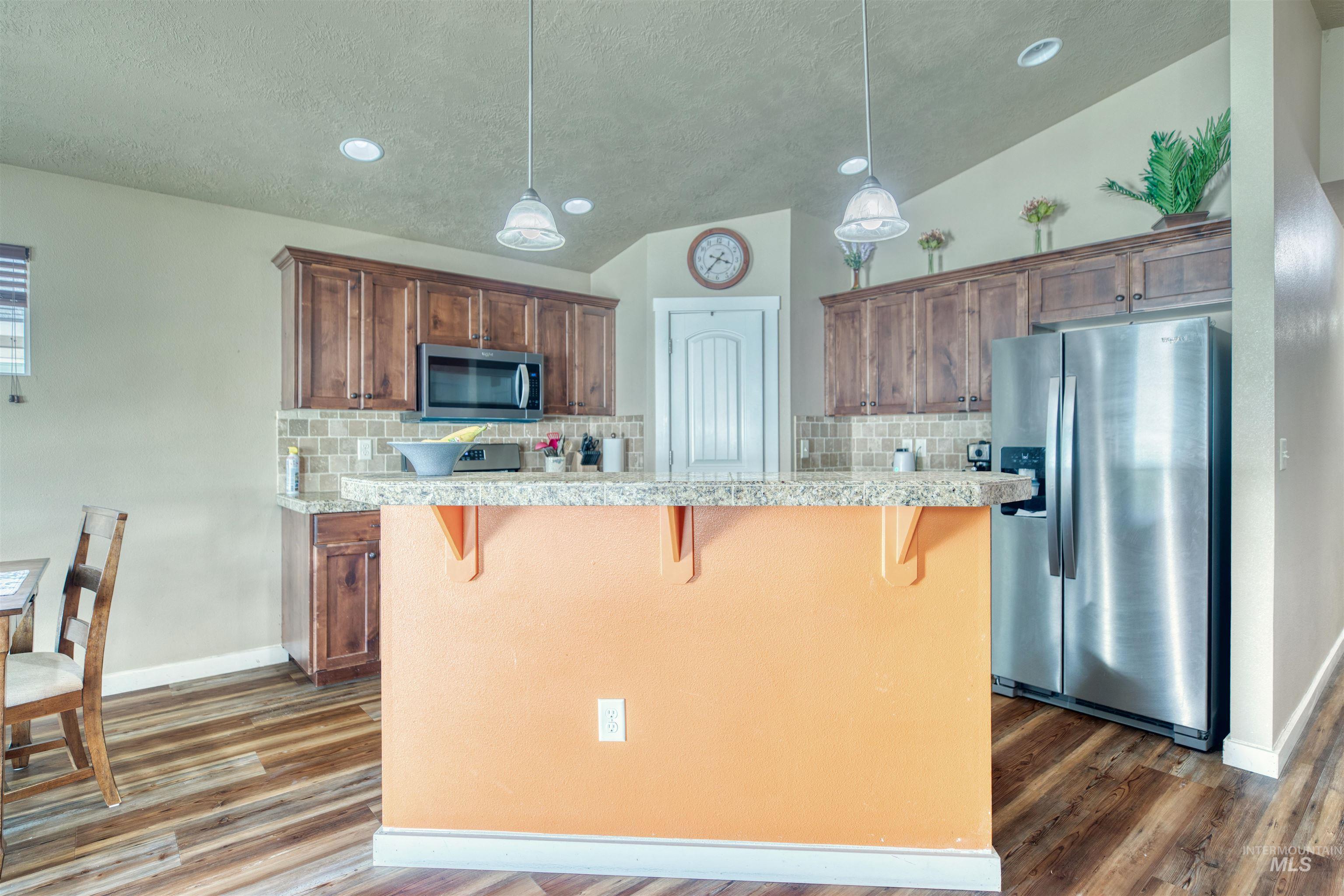 Kitchen with vaulted ceiling, stainless steel appliances, tasteful backsplash, a kitchen breakfast bar, and dark wood-style floors