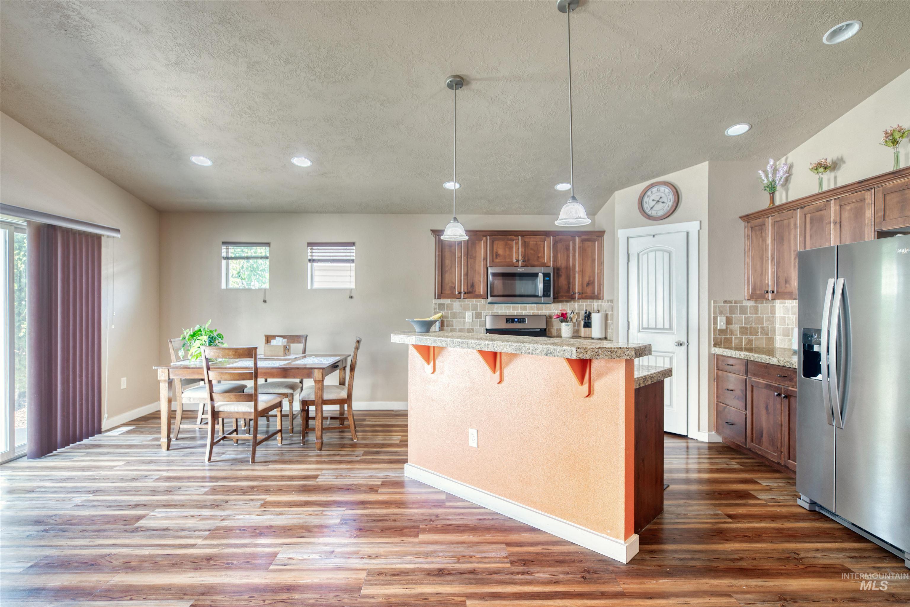 Kitchen with stainless steel appliances, a breakfast bar, recessed lighting, brown cabinets, and light countertops