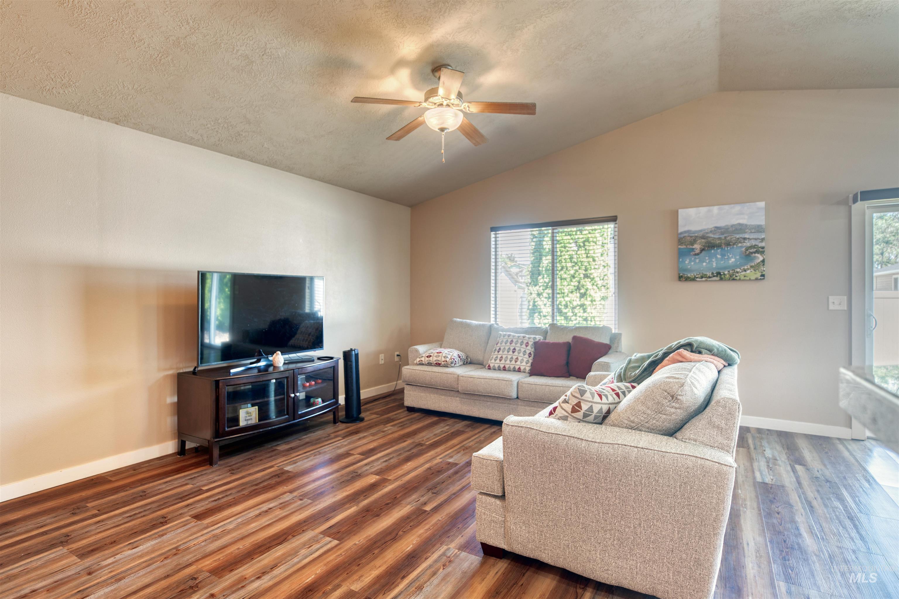 Living room with lofted ceiling, a ceiling fan, dark wood-style floors, and a textured ceiling
