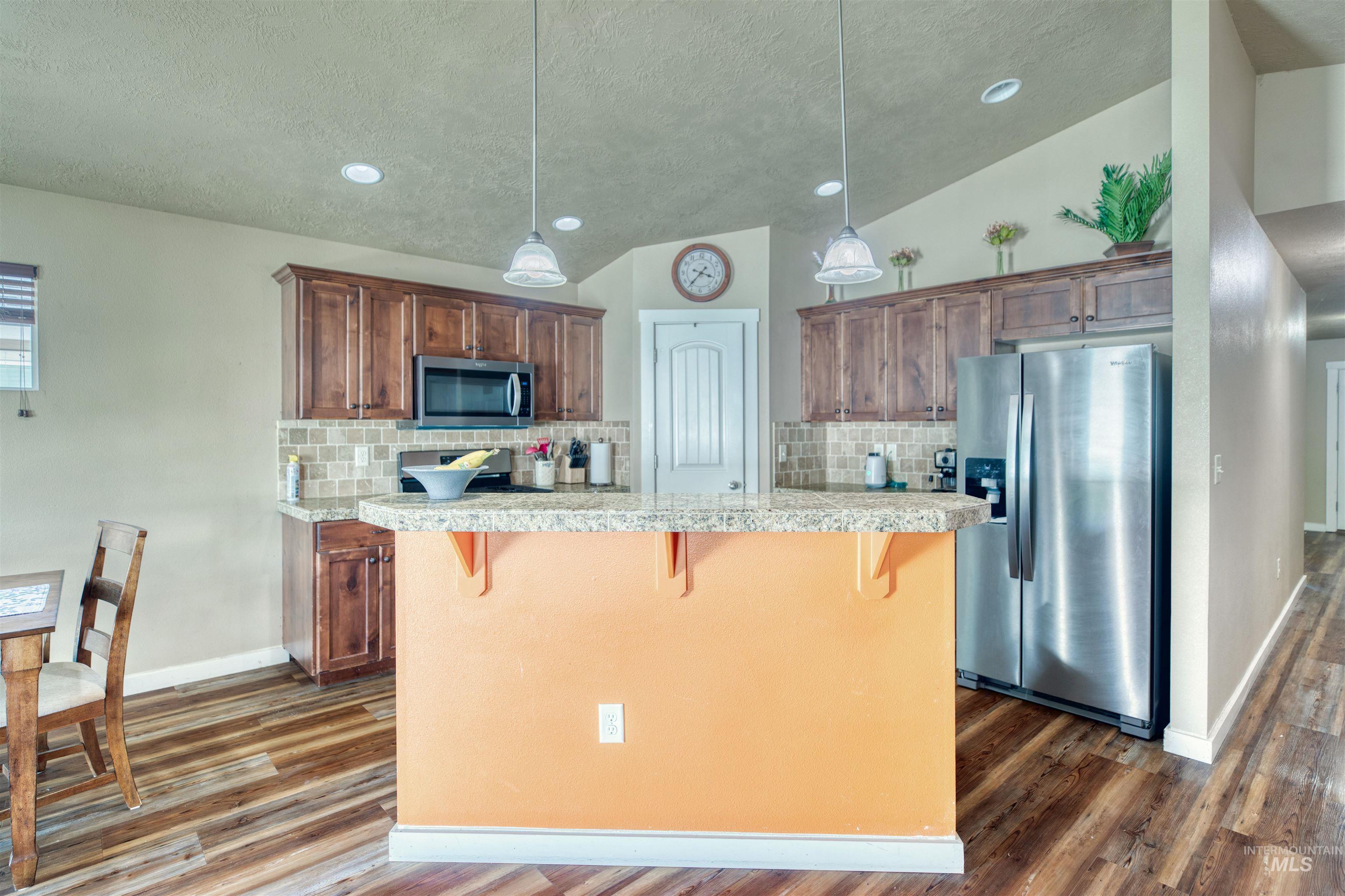 Kitchen with vaulted ceiling, stainless steel appliances, a breakfast bar area, dark wood finished floors, and decorative backsplash