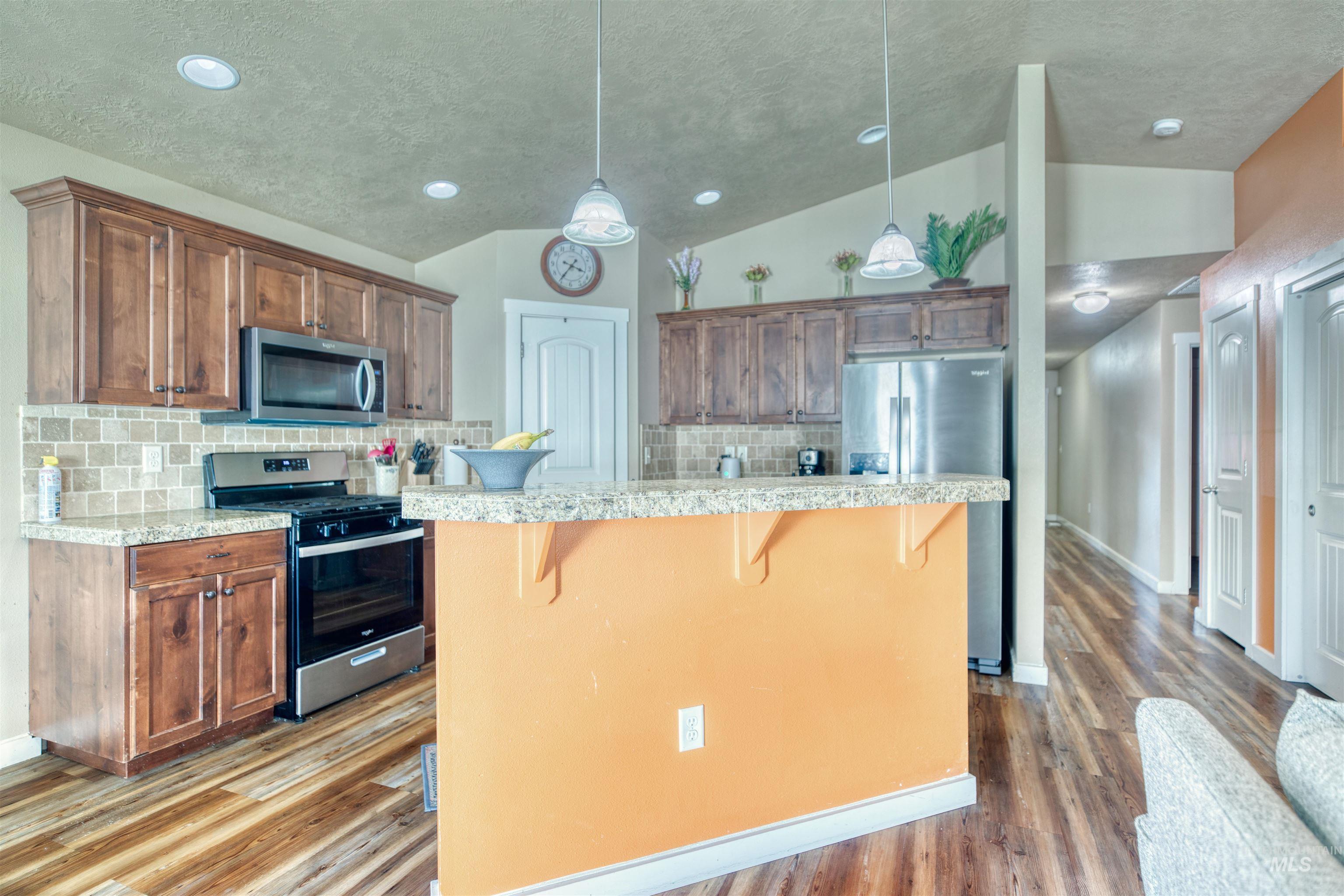 Kitchen featuring lofted ceiling, appliances with stainless steel finishes, a breakfast bar, tasteful backsplash, and decorative light fixtures
