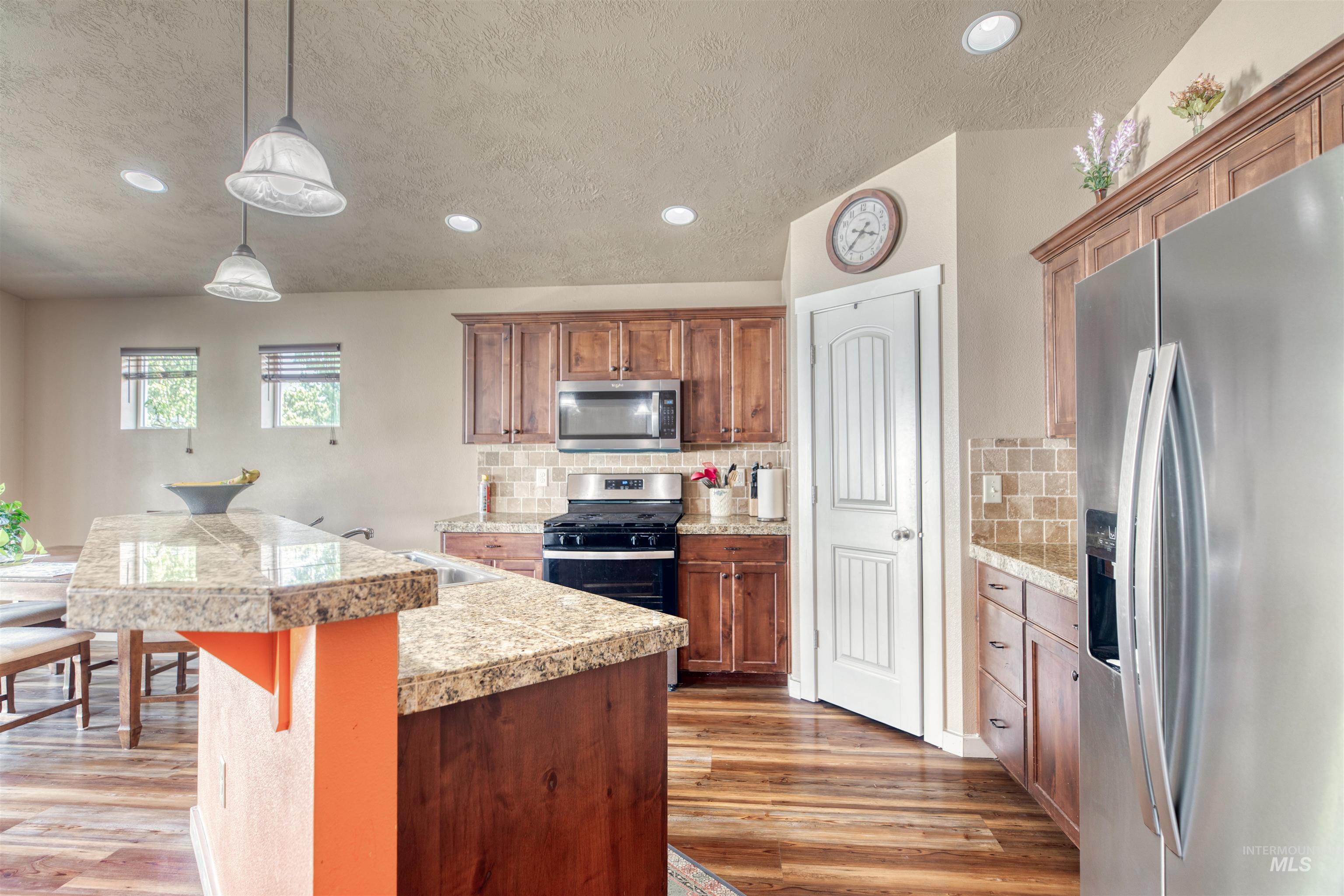 Kitchen with stainless steel appliances, recessed lighting, decorative backsplash, light wood-type flooring, and brown cabinets