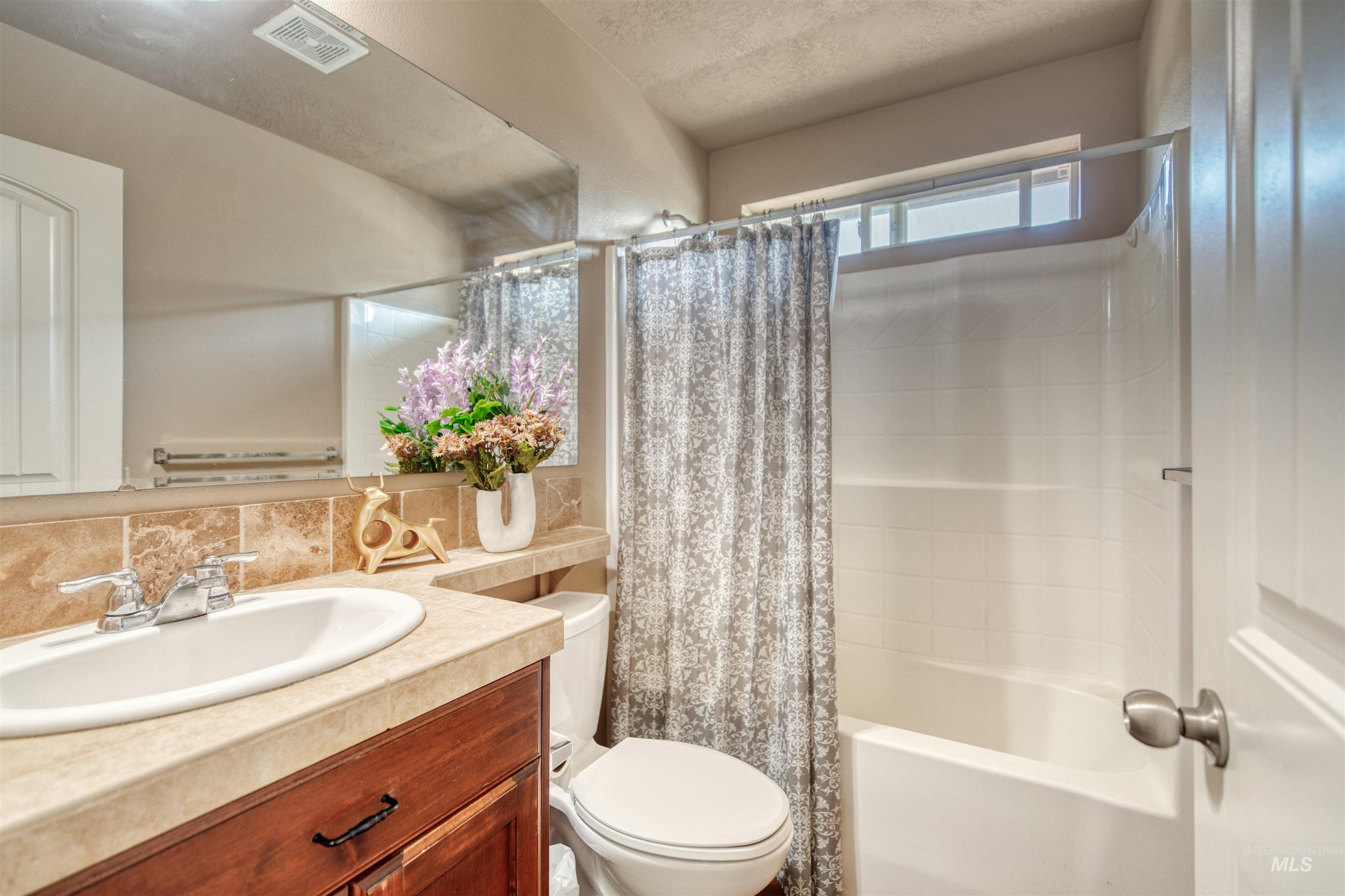 Full bathroom with vanity, shower / bath combo with shower curtain, tasteful backsplash, and a textured ceiling