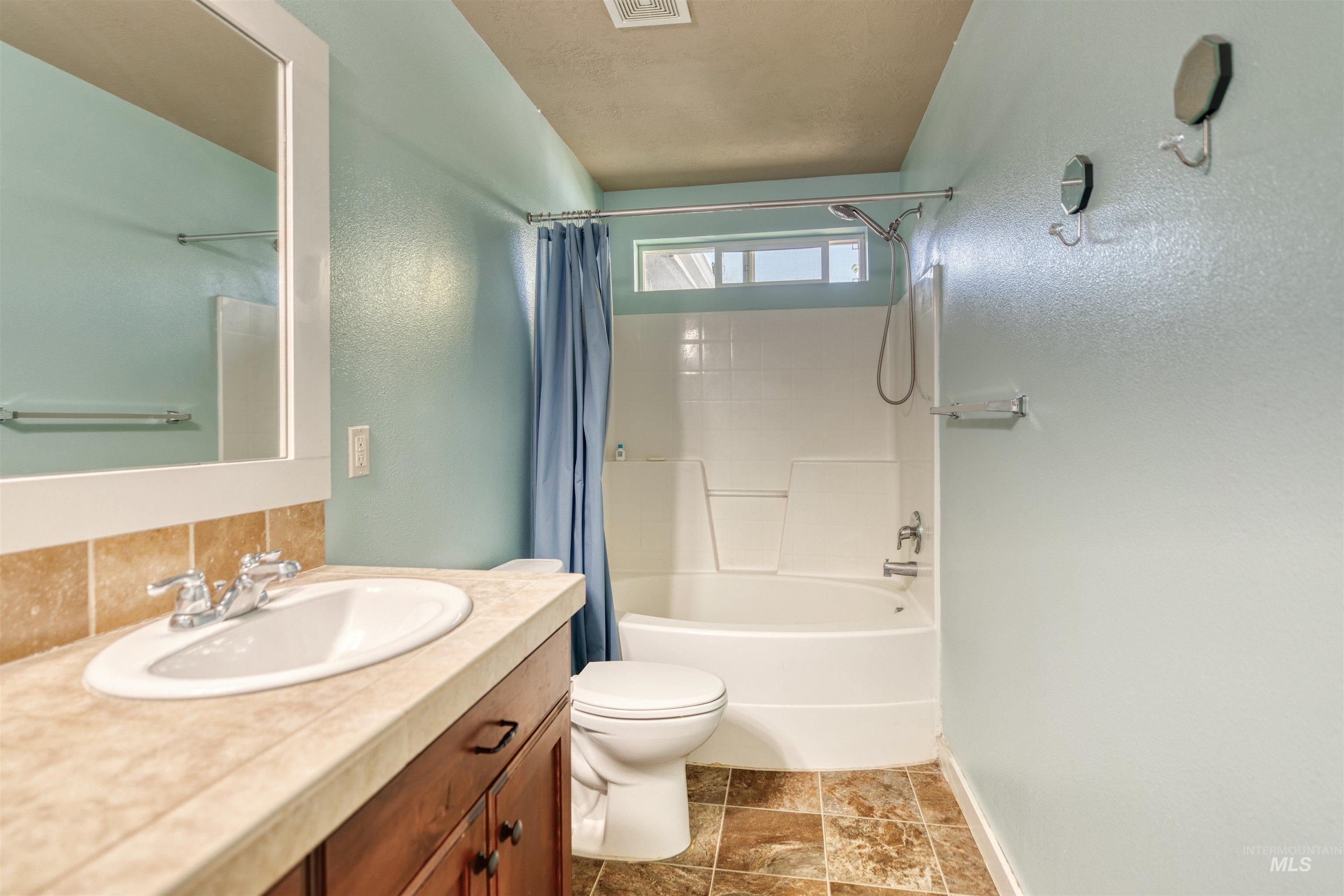 Bathroom featuring vanity, shower / bath combo, stone finish floors, and backsplash