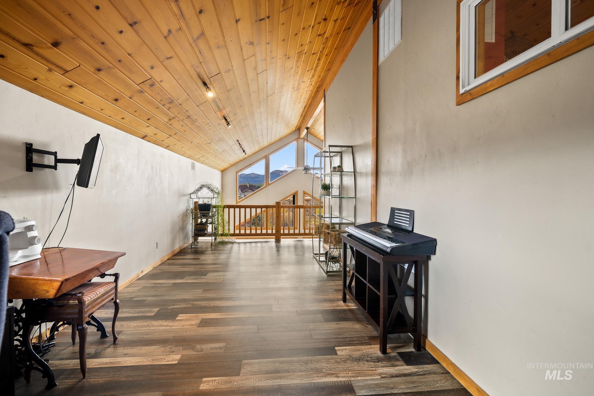 Living area featuring lofted ceiling, wooden ceiling, dark wood-type flooring, and an upstairs landing