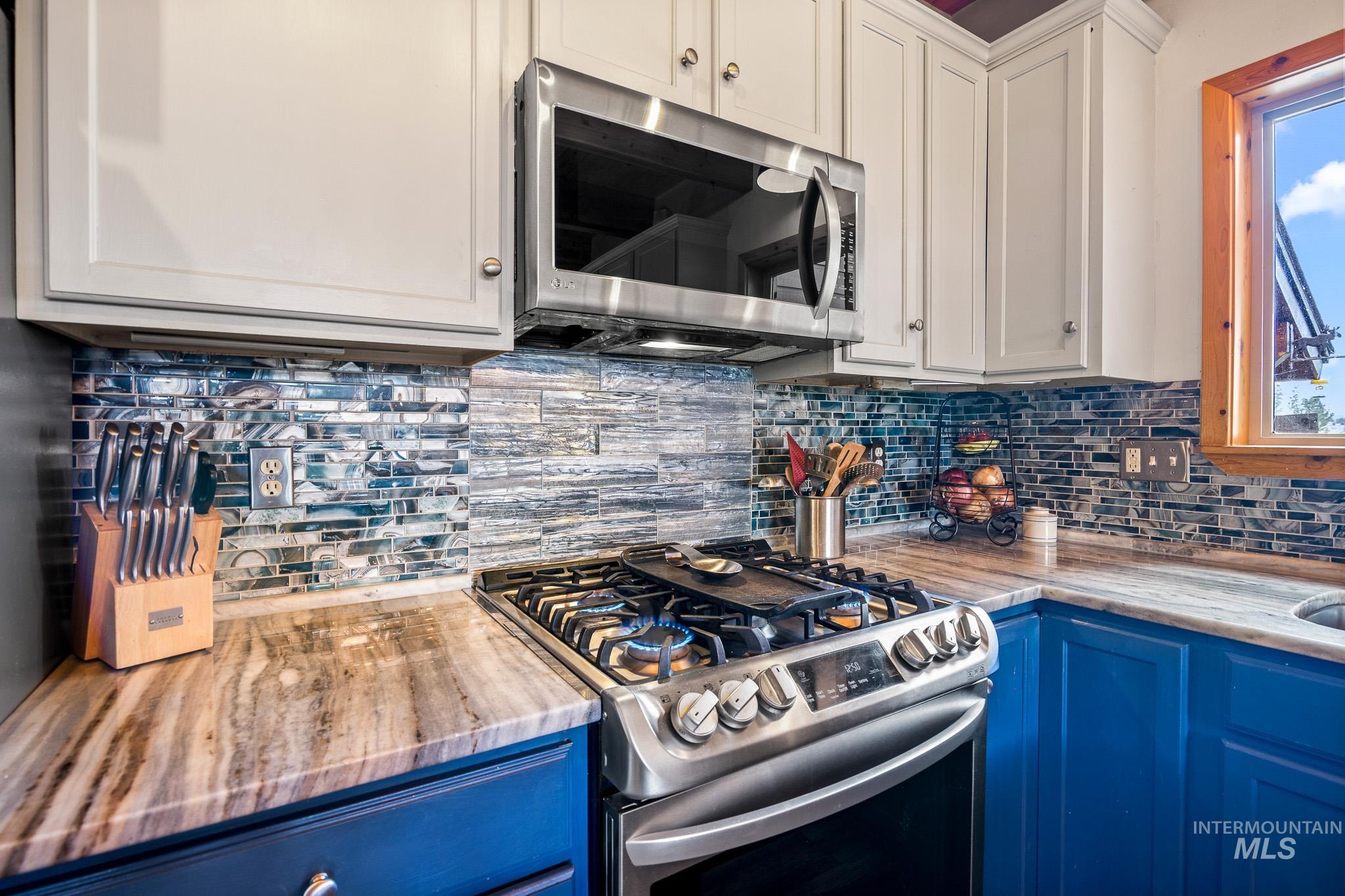 Kitchen with decorative backsplash, appliances with stainless steel finishes, blue cabinets, and white cabinetry