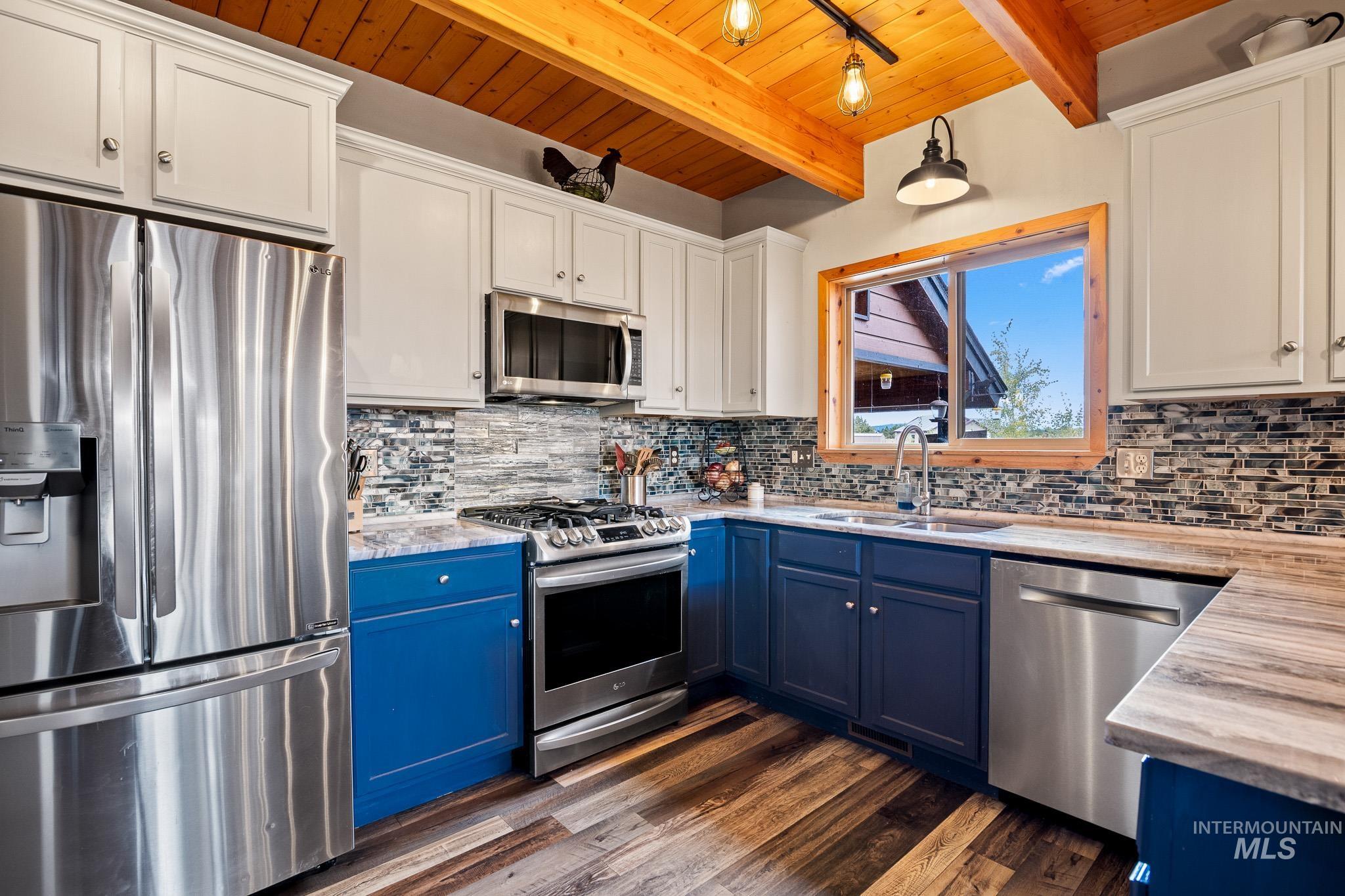 Kitchen featuring blue cabinetry, appliances with stainless steel finishes, a wooden ceiling with exposed beams, tasteful backsplash, and white cabinetry