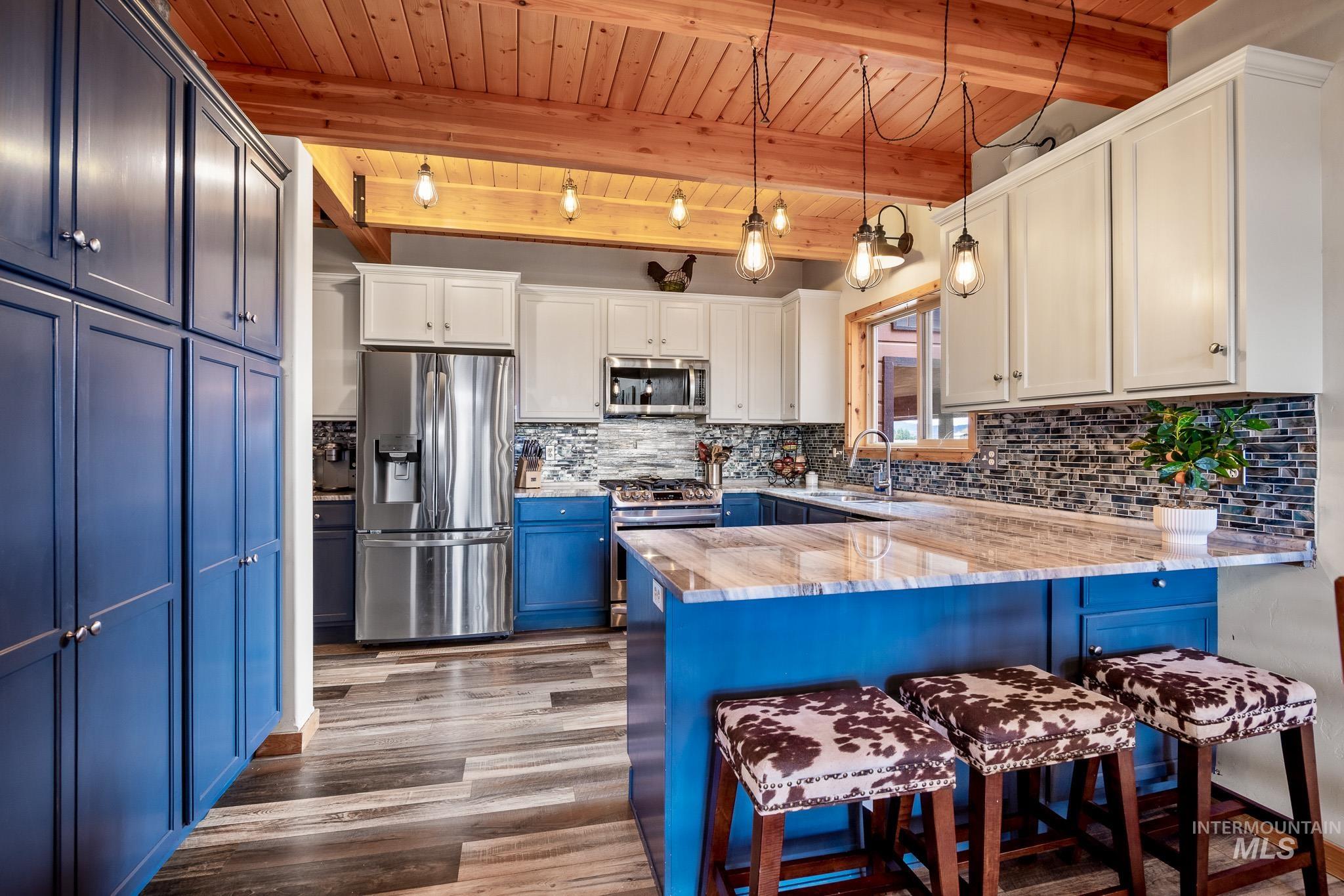 Kitchen with blue cabinetry, a kitchen breakfast bar, appliances with stainless steel finishes, a peninsula, and backsplash