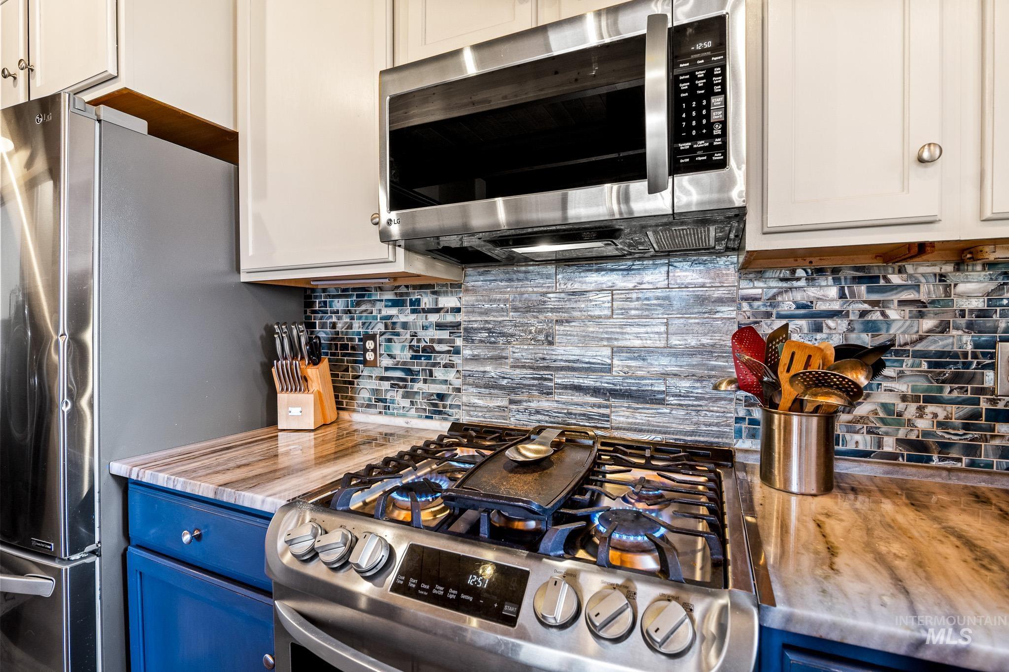 Kitchen with decorative backsplash, stainless steel appliances, and blue cabinets and gas range
