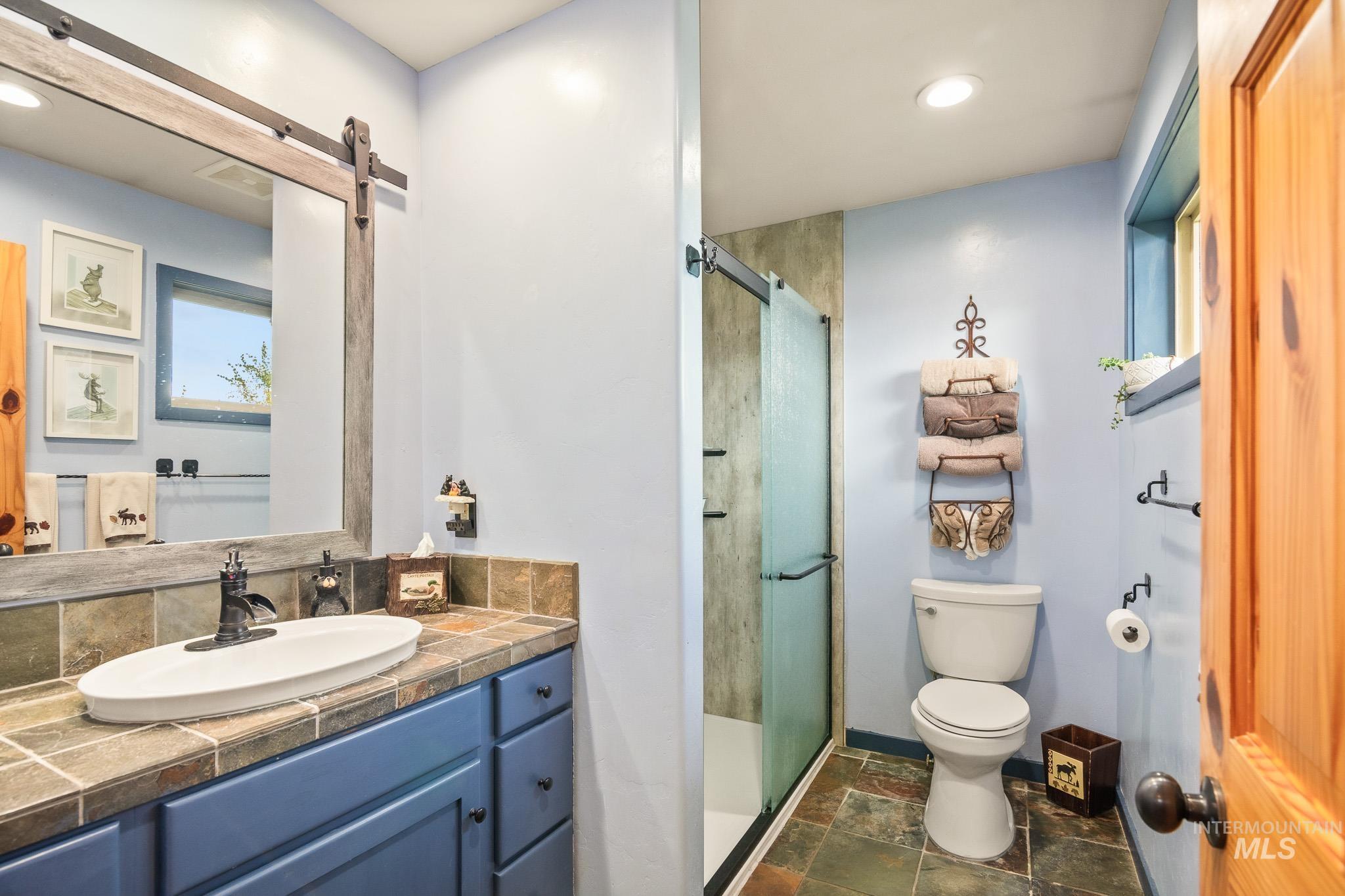 Full bath with a stall shower, vanity, recessed lighting, and dark stone finish floors
