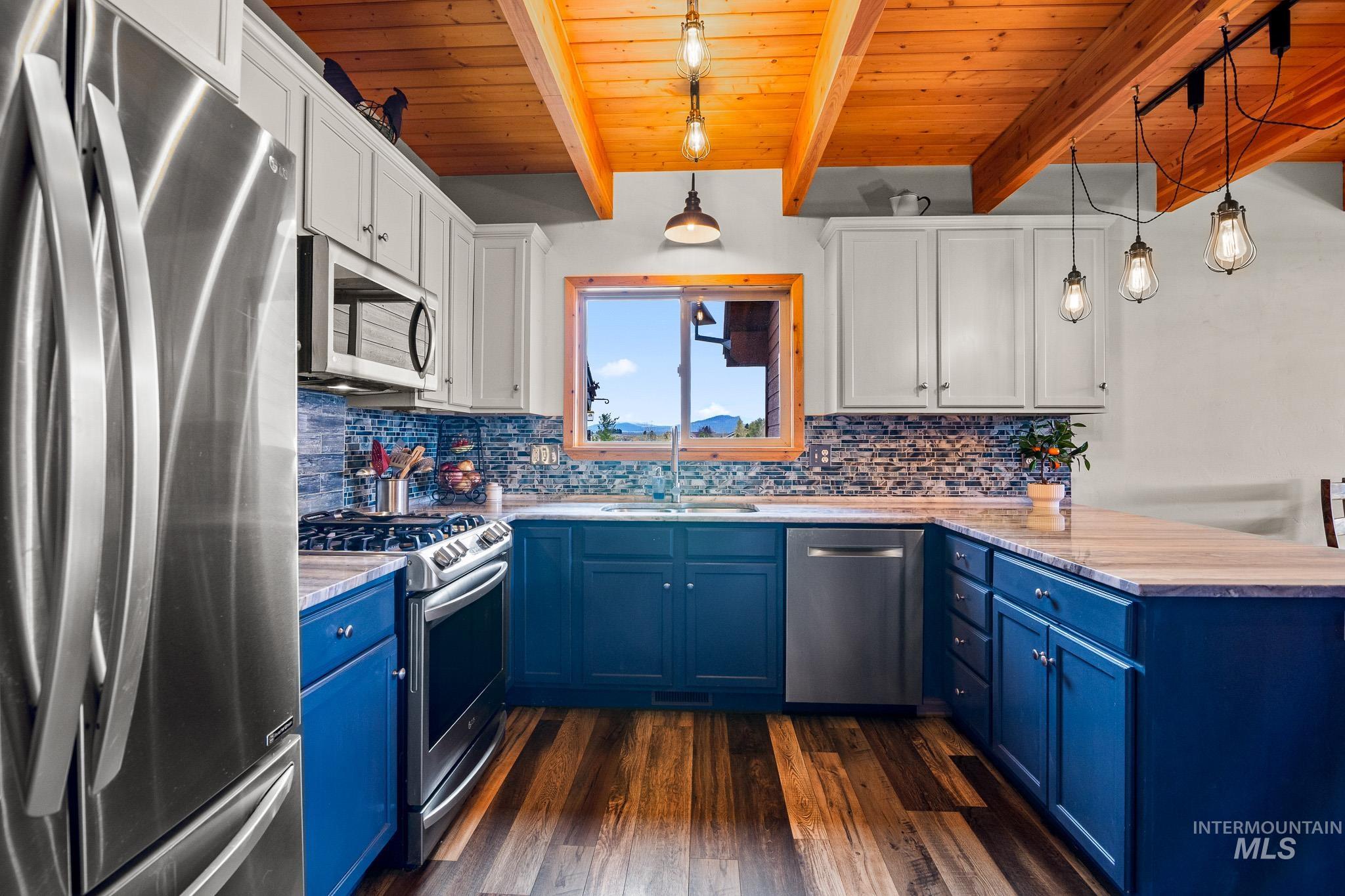 Kitchen featuring blue cabinets, stainless steel appliances, a peninsula, pendant lighting, and a wooden ceiling with exposed beams