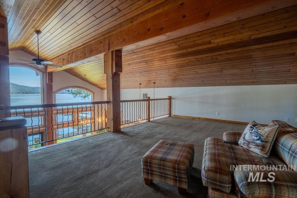 Loft area featuring plank wood ceiling, exposed wood beams, carpet flooring, and a decorative metal railing overlooking a wall of arched windows