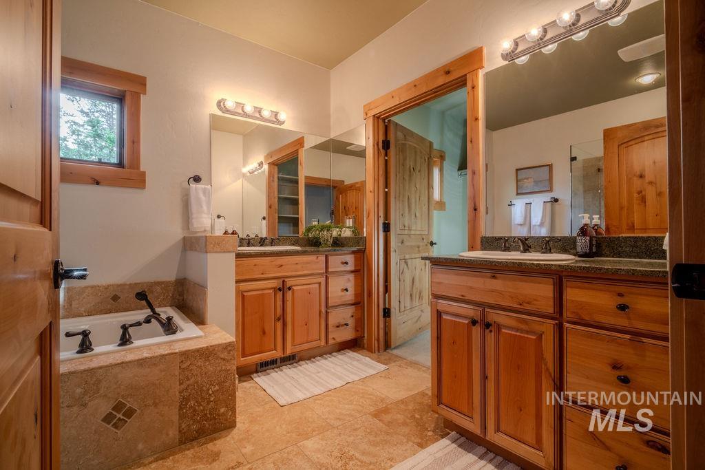 Bathroom featuring a built-in tub with tile surround, dual vanity with wood cabinetry, and extensive tile flooring