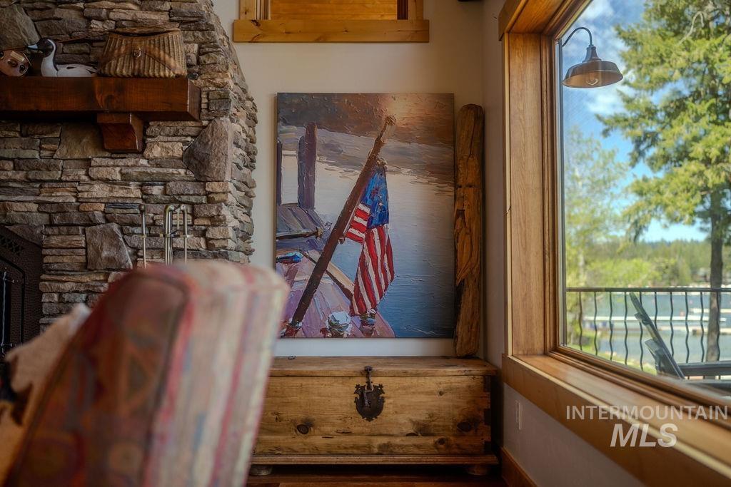 Expansive window offering water and tree scenery, featuring a stone fireplace with a substantial wood mantel, natural wood window trim, and a rustic wood chest