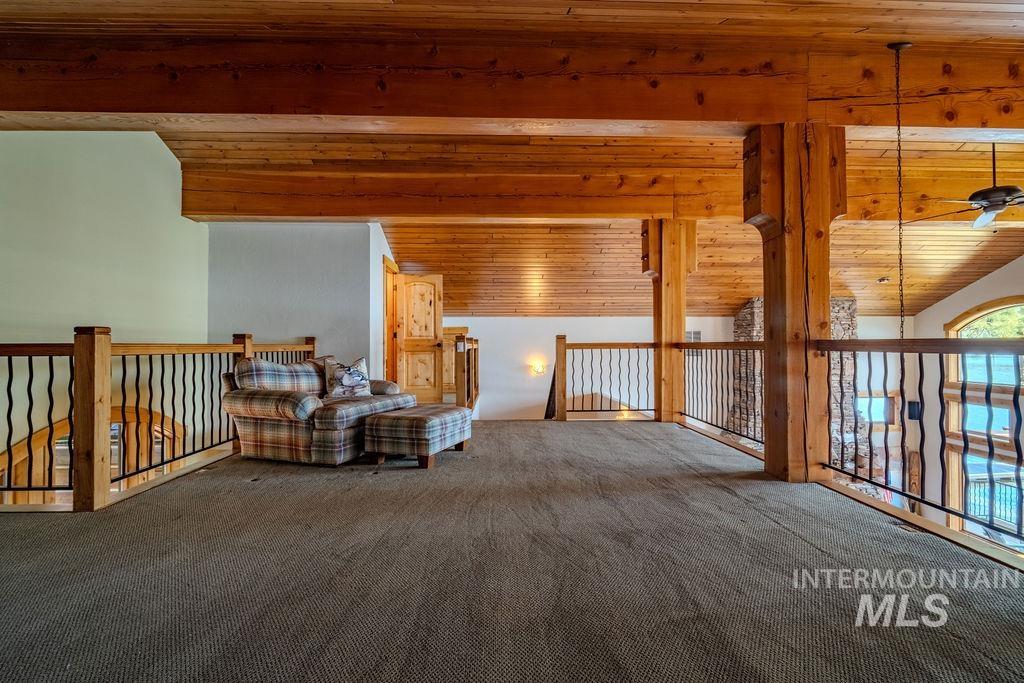 Expansive loft area featuring wood-finish ceiling, exposed structural beams, and wood railing with decorative metal balusters