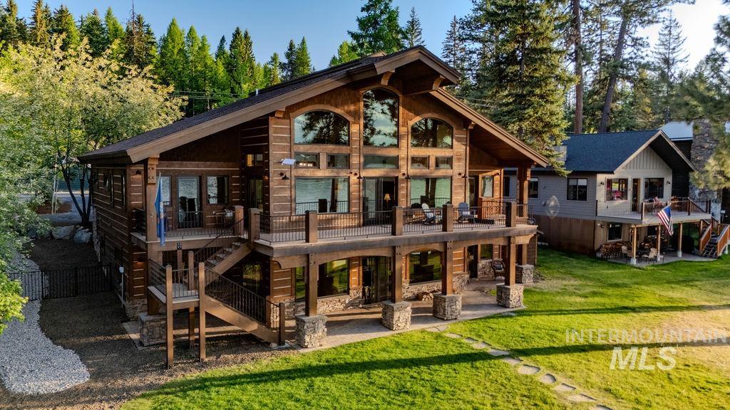 Rustic-style residence featuring a prominent wooden exterior, a spacious upper-level balcony, a stone-accented lower patio, large arched windows, and an external staircase with wrought iron railings