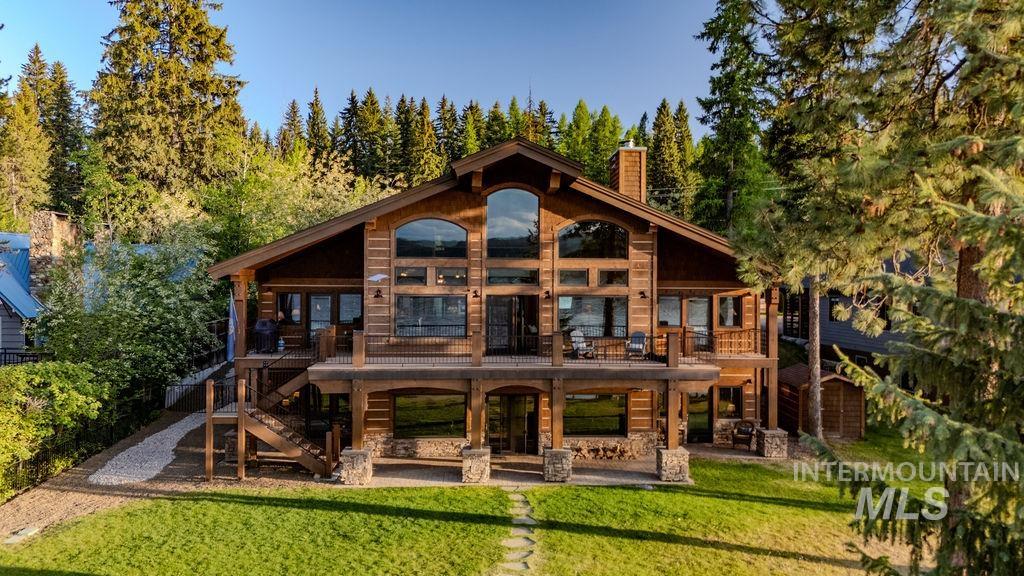 Expansive timber-frame residence featuring a gable roof, multiple balconies, a stone chimney, a lower-level patio, and large windows