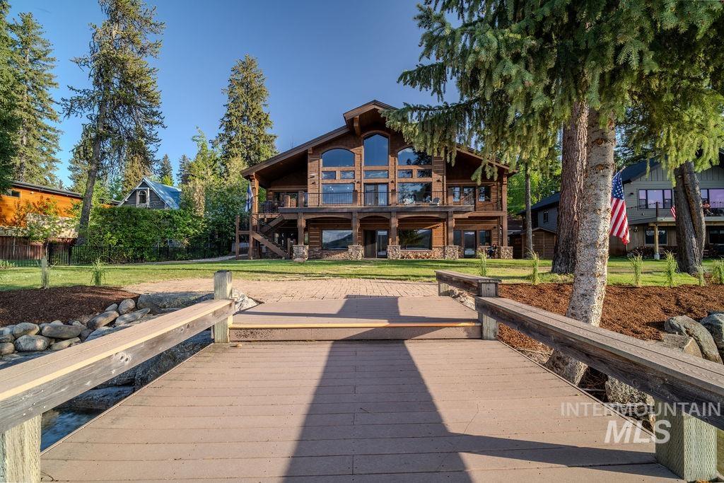 Expansive wood dock leading to a log-style residence featuring a stone foundation, prominent arched windows, a covered lower patio, and an upper balcony
