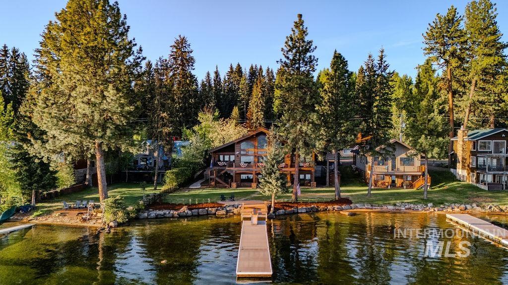 Waterfront property featuring a private dock, manicured lawn, mature trees, and a multi-level wood-clad exterior
