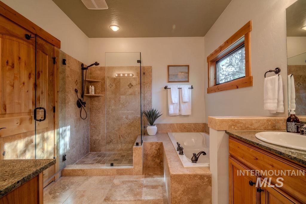 Expansive bathroom featuring a walk-in shower with tile surround, a built-in soaking tub, a single vanity with stone countertop, wood-finish cabinetry, and a window with wood trim