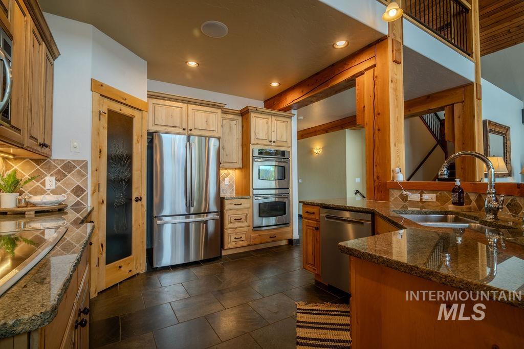 Kitchen featuring granite countertops, stainless steel appliances, wood cabinetry, stone tile flooring, and exposed timber beams