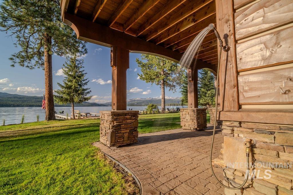 Outdoor shower with a natural wood surround and stone base, featuring a stamped concrete patio and a lush lawn