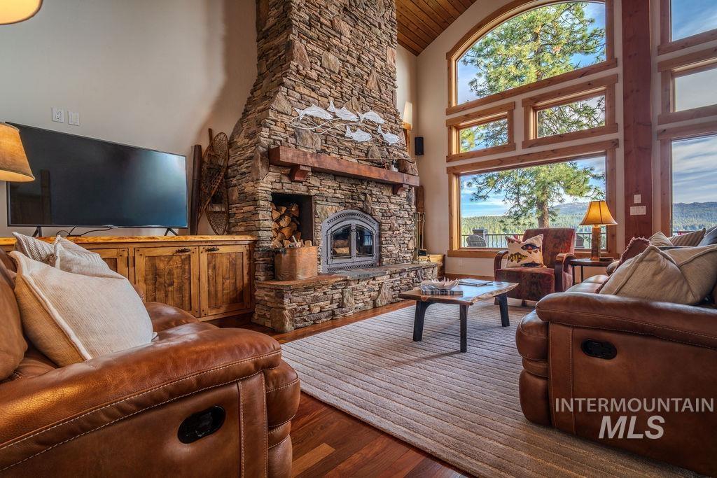 Stone fireplace with hearth, wood-finish flooring, vaulted ceiling with wood paneling, wood-framed picture windows, and a built-in media console