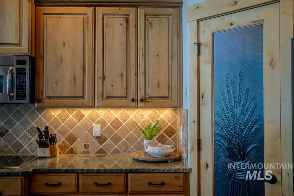 Kitchen counter space featuring wood-finish cabinetry, under-cabinet lighting, a patterned tile backsplash, and a dark countertop