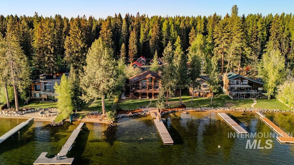 Waterfront property with multiple private docks, lush green landscaping, and mature trees bordering a dense forest
