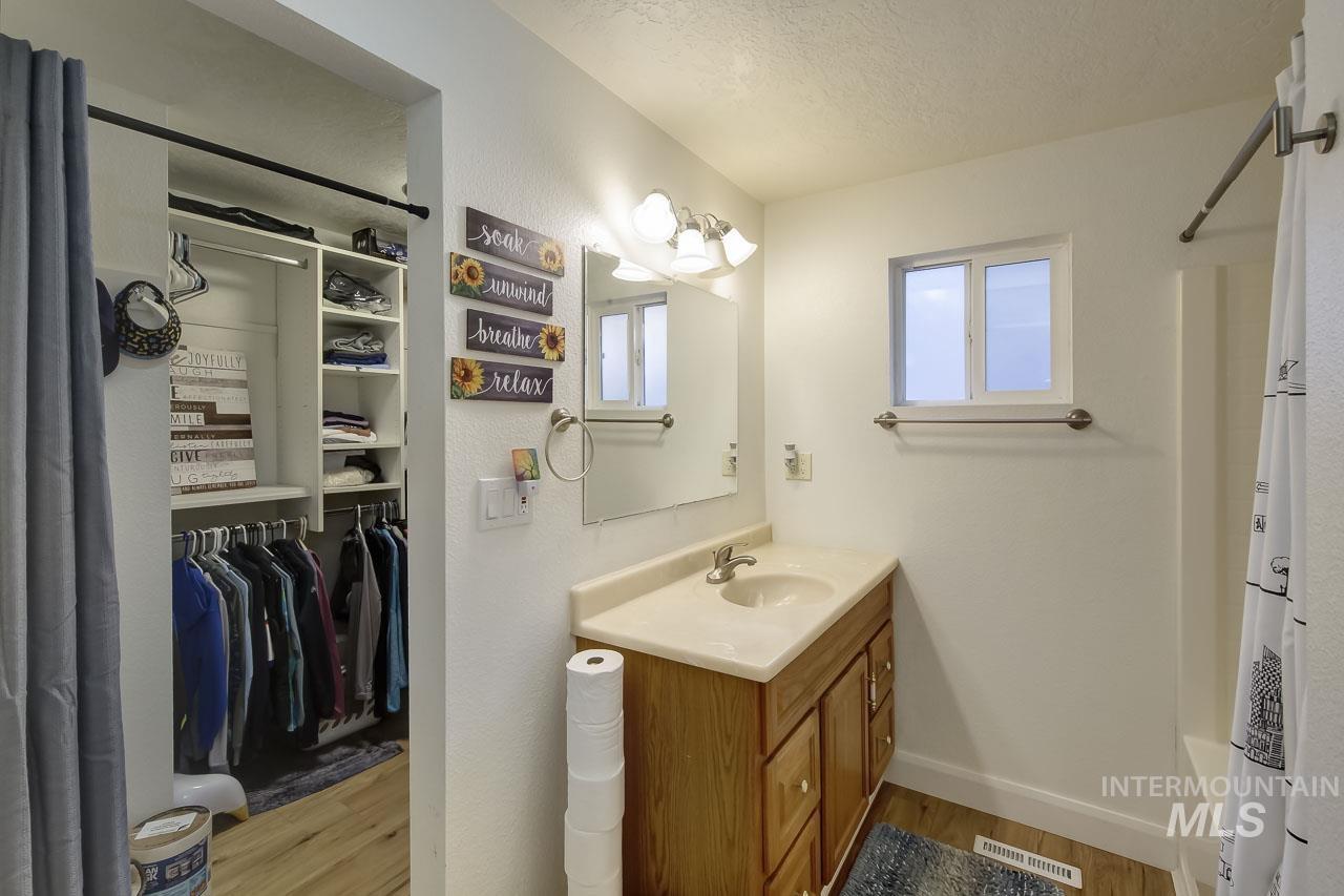Bathroom featuring light wood finished floors, vanity, a textured ceiling, a spacious closet, and shower / bathtub combination with curtain