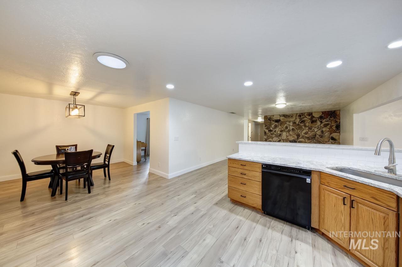 Kitchen featuring brown cabinetry, light stone counters, dishwasher, light wood-style floors, and hanging light fixtures