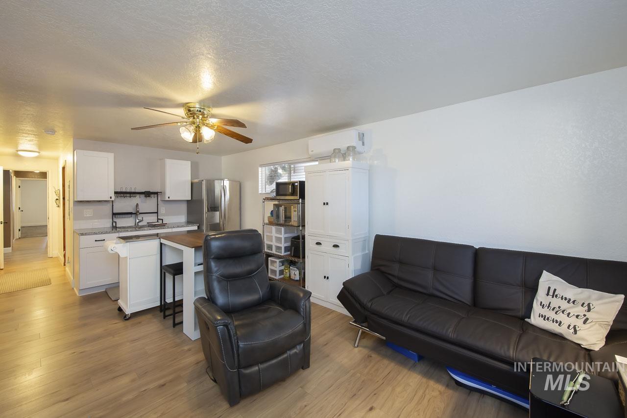 Living area featuring light wood-style flooring, a ceiling fan, a textured ceiling, and a wall unit AC