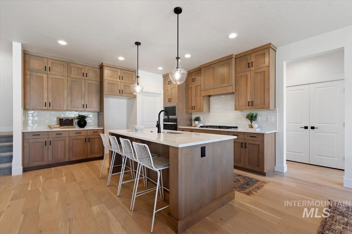 Kitchen with a kitchen breakfast bar, brown cabinets, a kitchen island with sink, light wood-style floors, and recessed lighting