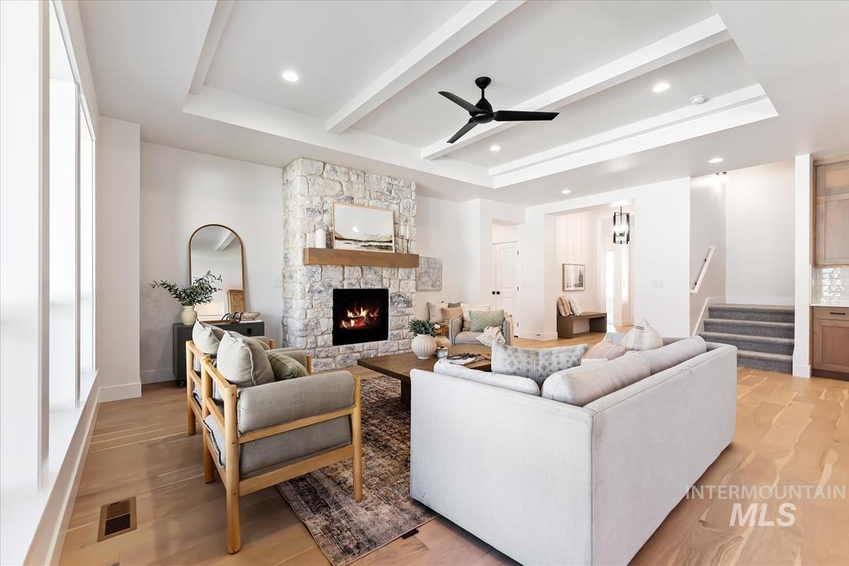 Living area with beam ceiling, a fireplace, a ceiling fan, stairs, and a raised ceiling