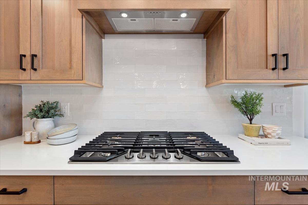 Kitchen view of range hood, backsplash, and stainless steel gas stovetop