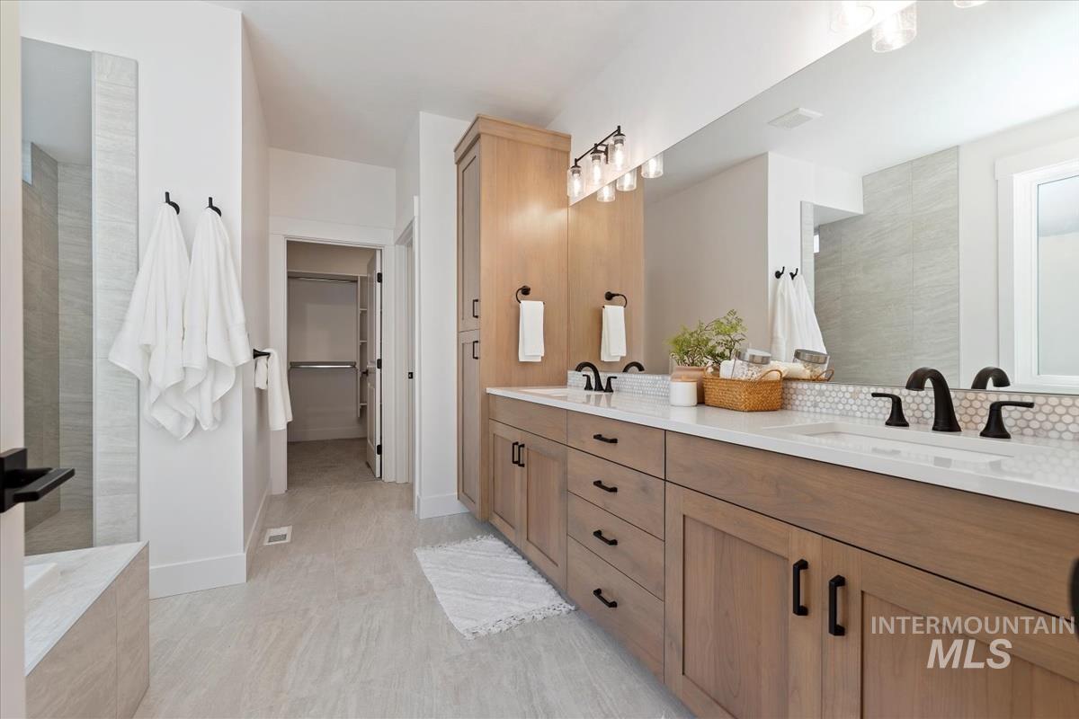 Full bath featuring double vanity, a spacious closet, a walk in shower, a tub, and tasteful backsplash