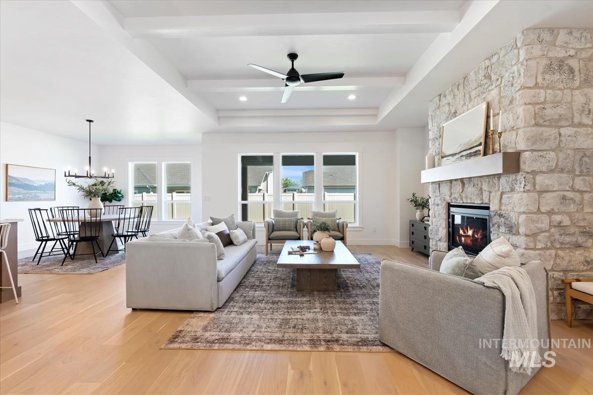 Living room with a fireplace, light wood-type flooring, beamed ceiling, a tray ceiling, and a chandelier