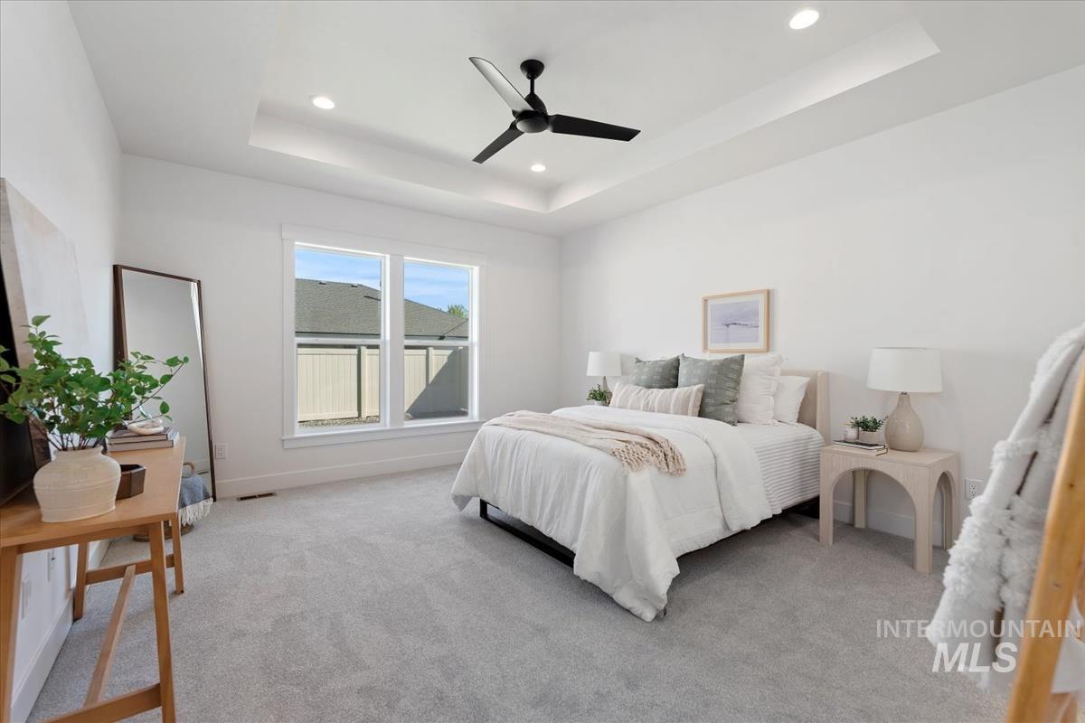 Bedroom with a raised ceiling, light colored carpet, ceiling fan, and recessed lighting