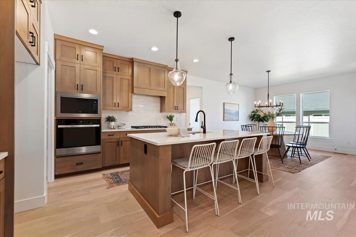 Kitchen featuring appliances with stainless steel finishes, pendant lighting, an island with sink, tasteful backsplash, and light wood-style floors