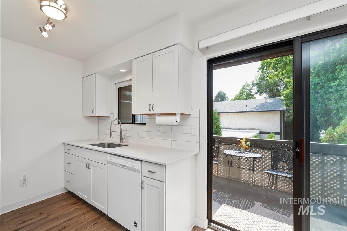 Kitchen with white cabinets, white dishwasher, dark wood-type flooring, decorative backsplash, and light stone countertops