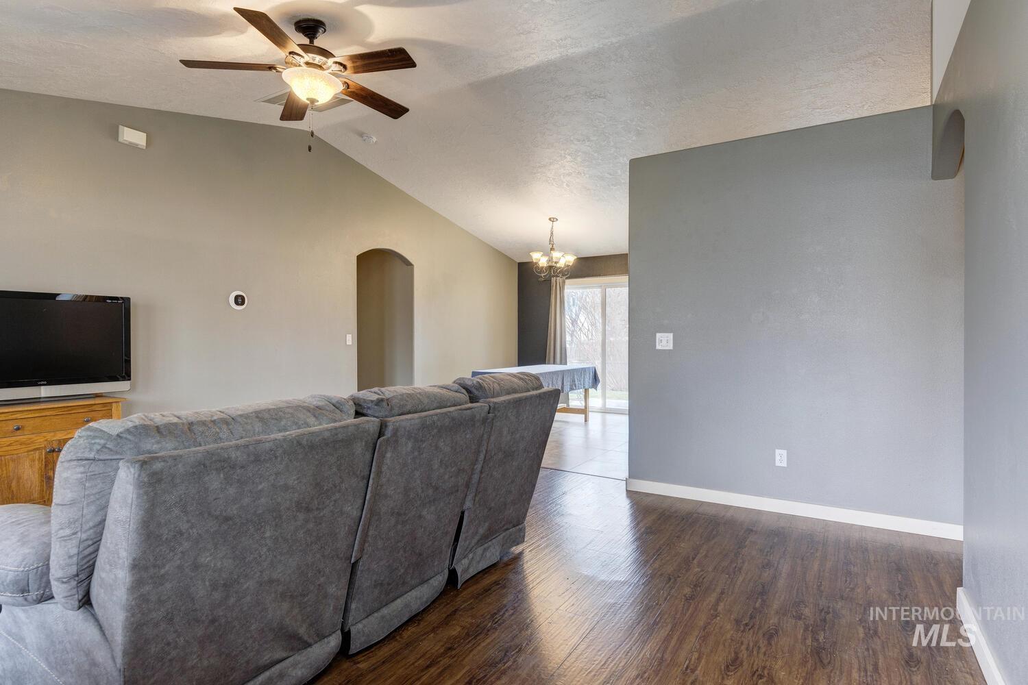 Living room with a chandelier, arched walkways, dark wood finished floors, a ceiling fan, and vaulted ceiling