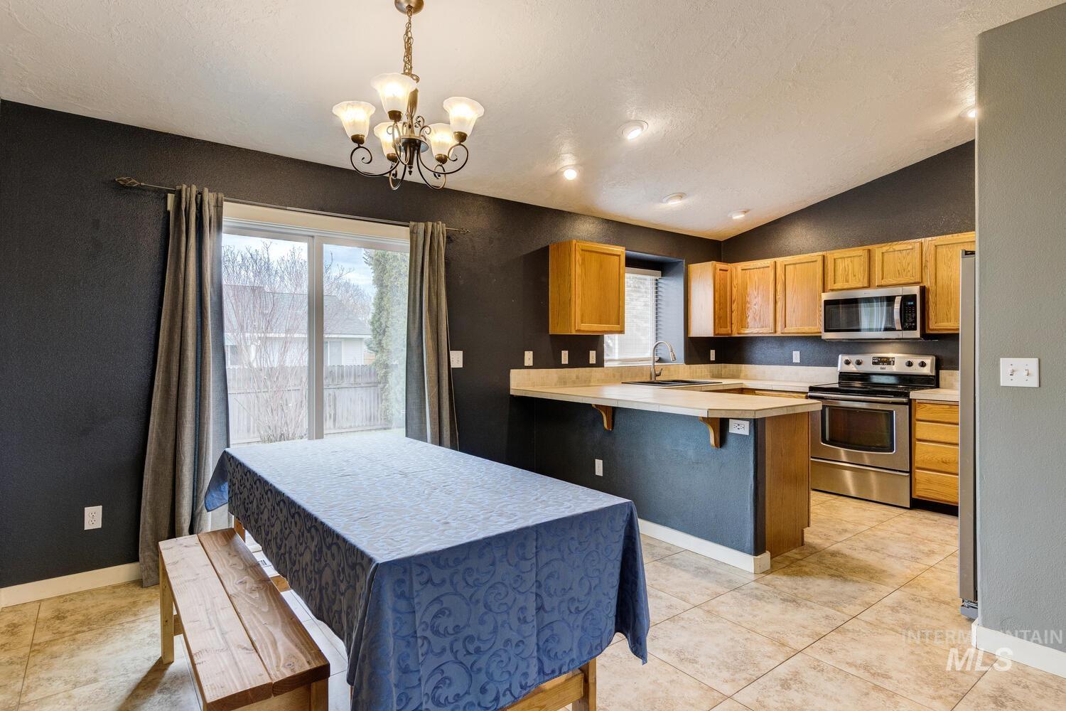 Kitchen featuring a breakfast bar, light countertops, stainless steel appliances, decorative light fixtures, and vaulted ceiling