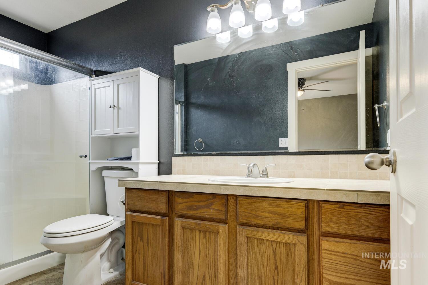 Bathroom with backsplash, vanity, a stall shower, and a ceiling fan