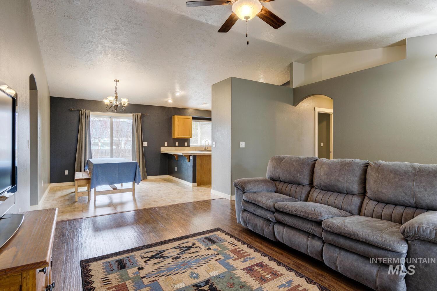 Living room featuring arched walkways, lofted ceiling, hardwood / wood-style flooring, a textured ceiling, and a ceiling fan