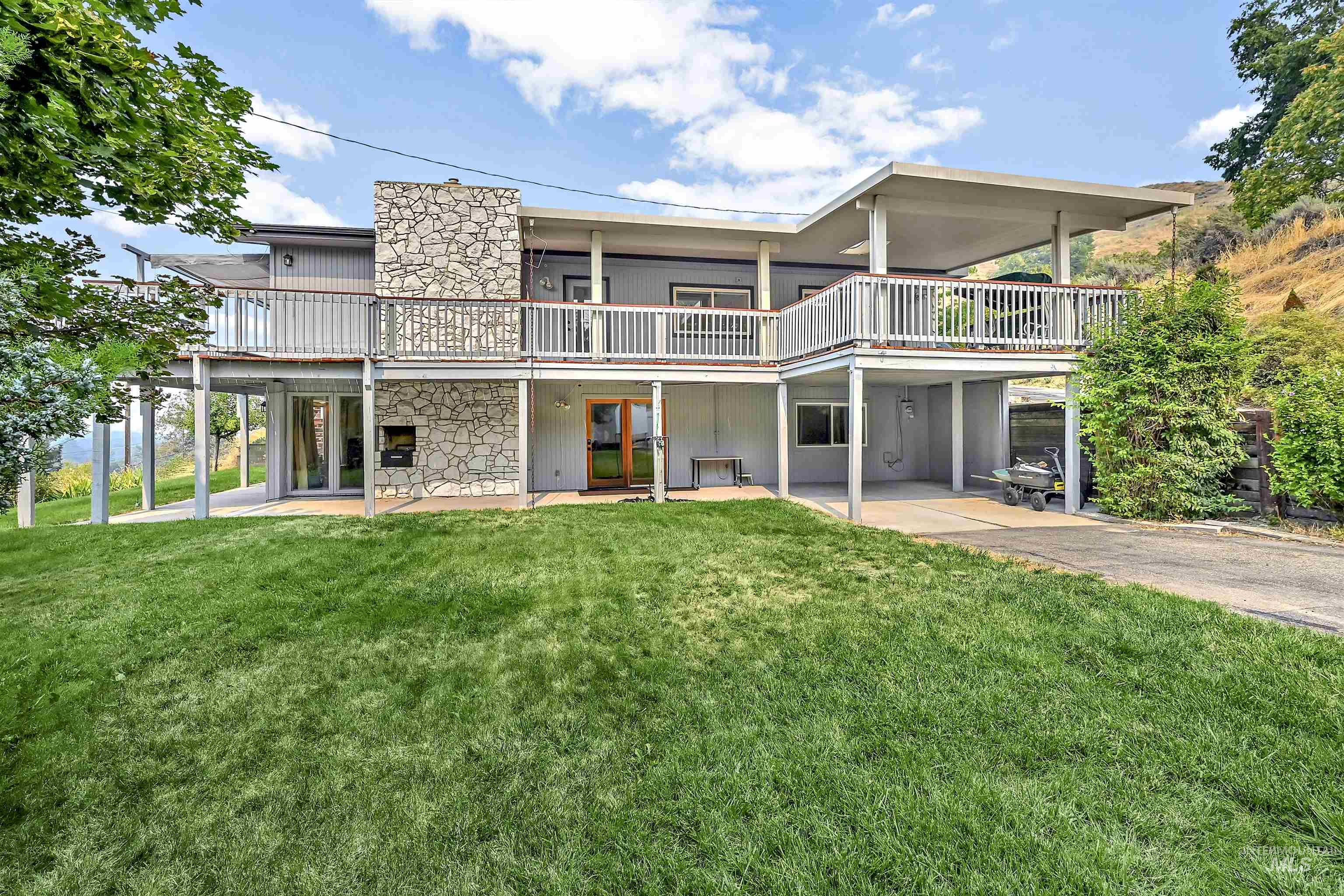 Rear view of house featuring a yard, a patio, and stone siding