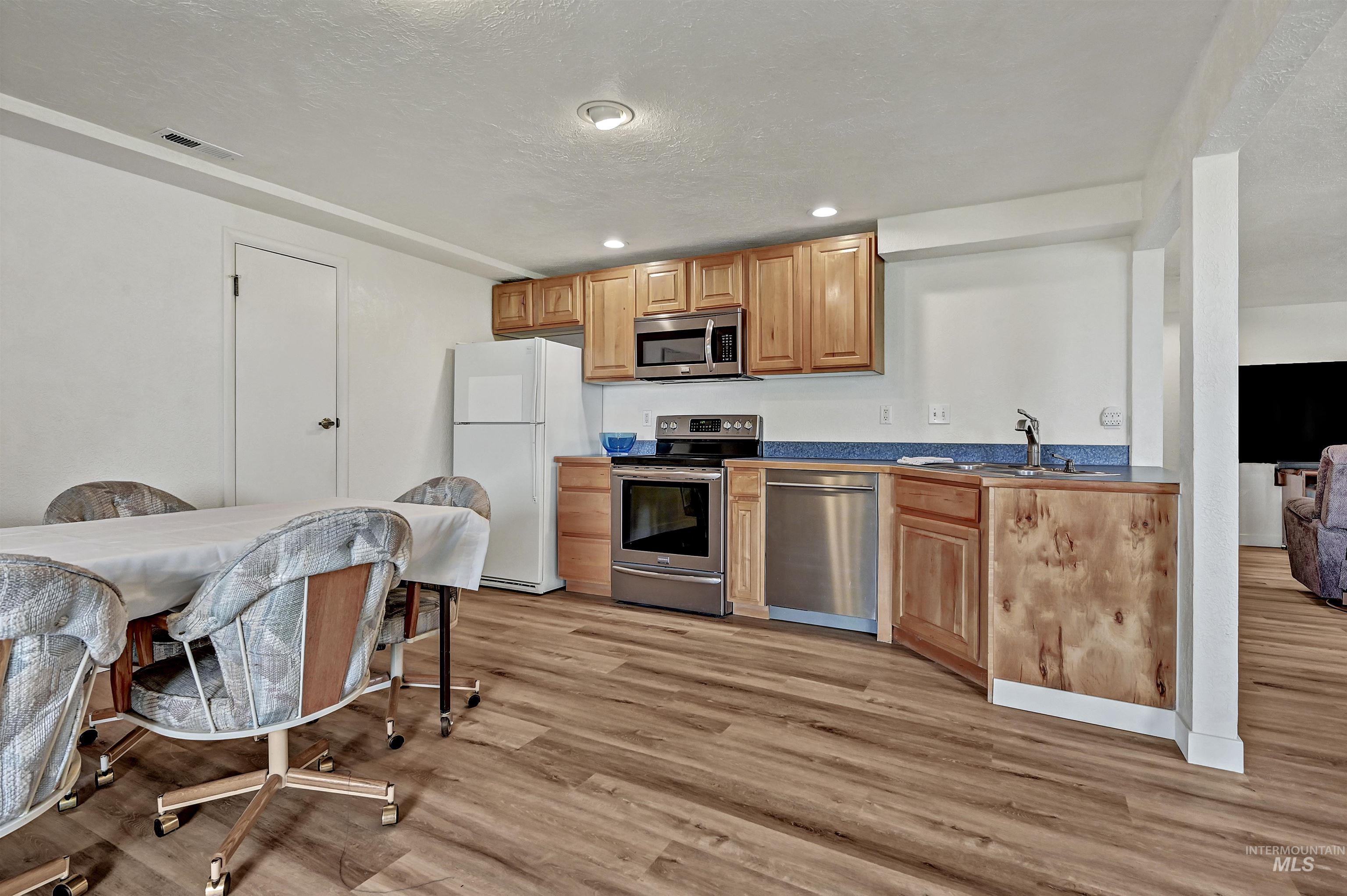 Kitchen with stainless steel appliances, light wood-type flooring, a textured ceiling, brown cabinetry, and recessed lighting