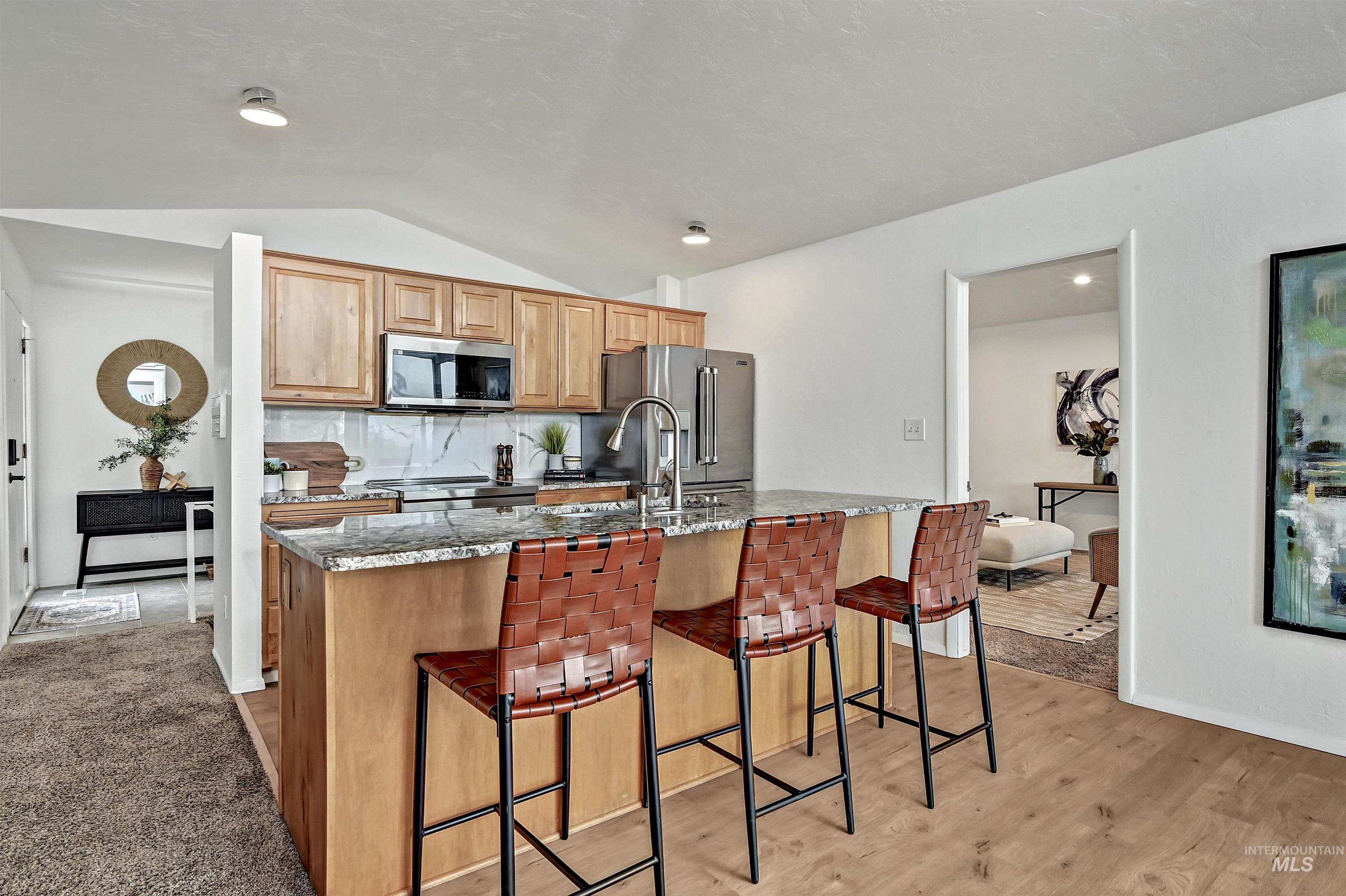 Kitchen with tasteful backsplash, dark stone countertops, a breakfast bar, lofted ceiling, and appliances with stainless steel finishes